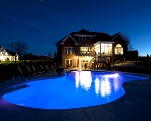 in-ground pool with night lights and fountain